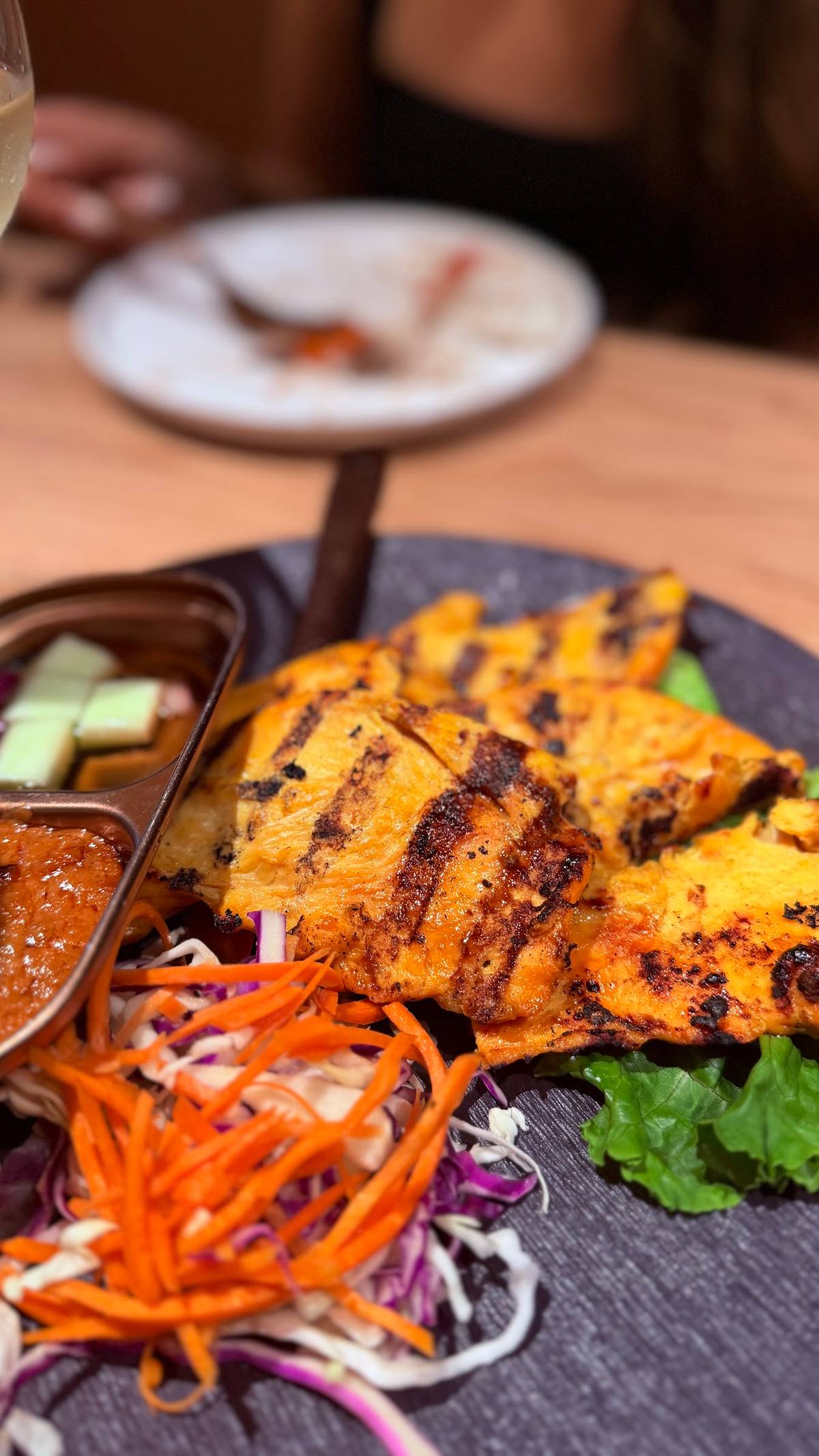 Close-up of the char-grilled chicken with grill marks, shredded carrot-and-cabbage slaw, and two dipping sauces.